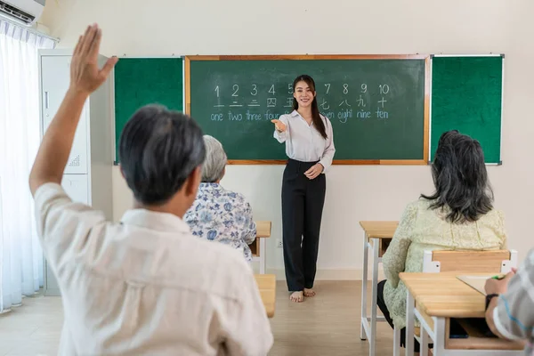 Asyalı bayan eğitmen, dil okulunda yetişkin öğrencilere ders veriyor. Çekici bayan öğretmen, yaşlıları özel ders sırasında yeni beceriler öğrenmeleri için teşvik ediyor..