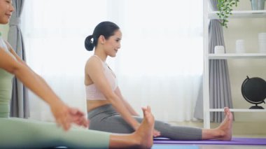 Genç Asyalı kadınlar gülümsüyor, yoga yapıyor, içeride bacaklarını açıyor..
