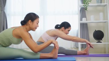 İki Asyalı kadın içeride minderlerin üzerinde yoga yapıyor..