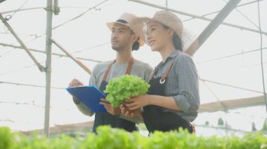 Asyalı kadın ve erkek seradaki bitkileri inceliyor.