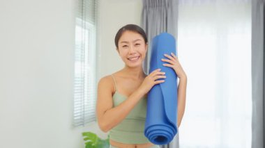 Elinde mavi yoga minderiyle gülümseyen Asyalı kadın..