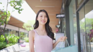 Marketin önünde elinde alışveriş çantası tutan genç Asyalı kadın..