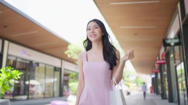 Alışveriş çantalı genç Asyalı kadın dükkanın önünde yürüyor..