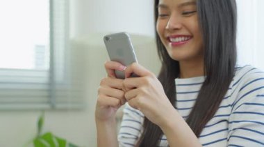 Genç Asyalı kadın akıllı telefon tutuyor, gülümsüyor, gülüyor, içeriyi inceliyor..