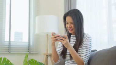 Akıllı telefon oyunu oynarken oturup gülümseyen genç bir kadın.