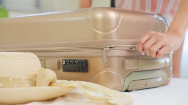 Genç bir kadın valizini topluyor ve şapkasını alıyor, yolculuk için hazır.