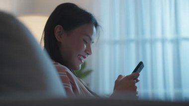 İçerde akıllı telefon kullanan Asyalı genç bir kadın gülümsüyor..