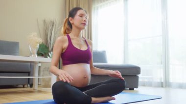 Evde yoga yapan hamile bir kadın yoga minderinde meditasyon yapıyor.