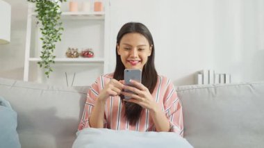 İçerde akıllı telefon kullanan Asyalı genç bir kadın gülümsüyor..