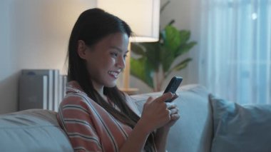 İçerde akıllı telefon kullanan Asyalı genç bir kadın gülümsüyor..