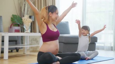 Hamile genç Asyalı kadın evde küçük bir kızla yoga yapıyor..