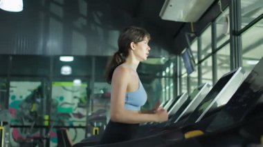 Spor salonunda koşu bandında koşan genç bir kadın..