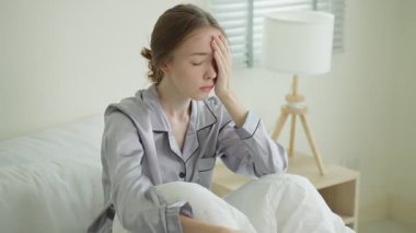 Yatakta oturan genç bir kadın, üzgün görünüyor..