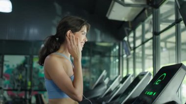 Spor salonunda koşu bandı kullanan genç bir kadın..