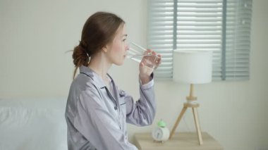 Genç Asyalı kadın evde otururken su içiyor..