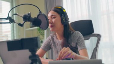 Genç Asyalı kadın mikrofon masasında ses kaydı yapıyor.