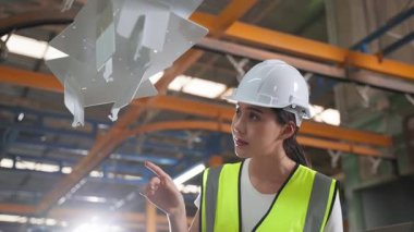 Fabrikanın içindeki makineleri denetleyen kasklı genç bir kadın..