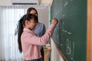 İlkokuldaki sınıfta Asyalı bir öğrenci öğretmeniyle birlikte öğreniyor. Sevimli genç kız öğrenciler gemide bayan öğretmenlerle birlikte yazıyor, eğitiyor ve sınıftaki dersi anlatıyor..