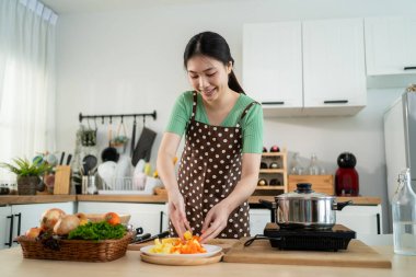 Asyalı genç bir kadın sabah evde mutfakta sağlıklı yemekler pişiriyor. Çekici kadın ev hanımı kendini mutlu hissediyor ve evde kahvaltıda çorba yapmak için malzemeler hazırlamaktan zevk alıyor..