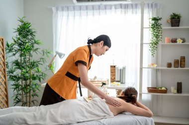 Asyalı genç bir kadın güzellik merkezinde sırt masajı yaptırıyor. Çekici, güzel bir kız masaj yatağında uzanıyor ve masaj salonundaki vücut için masözden rahatlatıcı fizyoterapi hizmeti alıyor.