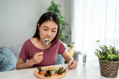 Asyalı genç bir kadın evdeki oturma odasında Vietnam böreği yiyor. Çekici, güzel bir kız masaya oturur, sabah evde sağlık için temiz aperatiflerin tadını çıkarır. Diyet ve Sağlıklı Yemek Konsepti