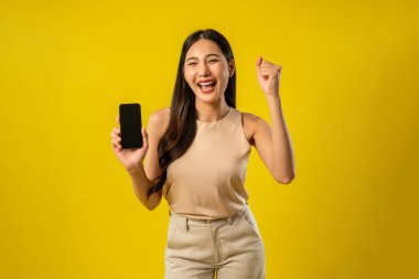 İzole edilmiş sarı arka planda akıllı telefonu tutan Asyalı kadının portresi. Çekici genç kız manken stüdyo ekranında çevrimiçi dijital cep telefonu aygıtı kullanırken mutlu ve neşeli hisseder..