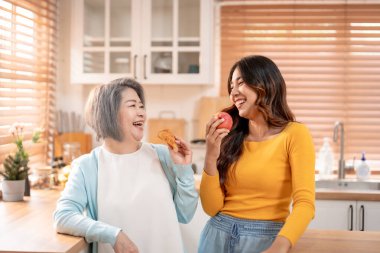 Asyalı yaşlı anne evde kızıyla birlikte mutfakta duruyor. Çekici genç torun ve büyükanne mutlu ve rahatlamış hissediyorlar. Sağlıklı meyveleri tutuyorlar ve birbirlerine bakıyorlar.