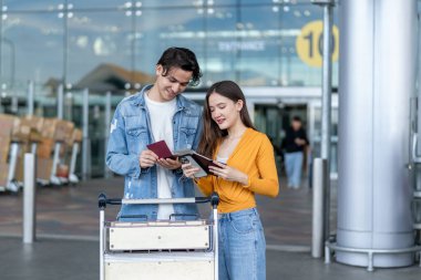 Havaalanı terminalinde birbirlerini selamlayan Asyalı genç çift. Çekici erkek ve kadın arkadaşlar tatil gezisi için uçakla yurtdışına gittikleri için mutlu ve heyecanlı hissediyorlar..