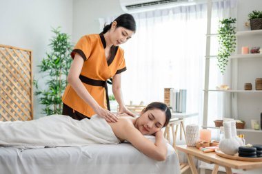 Asyalı genç bir kadın güzellik merkezinde sırt masajı yaptırıyor. Çekici, güzel bir kız masaj yatağında uzanıyor ve masaj salonundaki vücut için masözden rahatlatıcı fizyoterapi hizmeti alıyor.