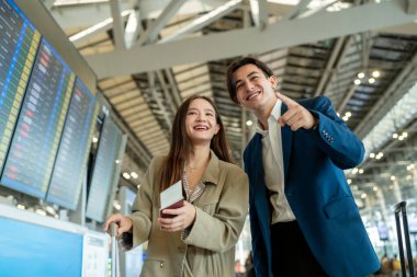 Asyalı işadamı ve kadın havaalanı terminalinden biniş kapısına doğru yürüyorlar. Çekici genç çift, tatil gezisi için uçakla yurtdışına giderken mutlu ve heyecanlı hissediyorlar..