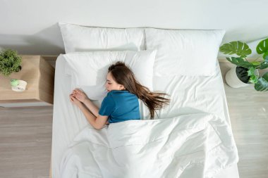 Asyalı güzel bir kadın sabahları yatak odasında yatağa uzanıyor. Çekici genç kız kendini mutlu ve rahat hissediyor, rahat bir yastık ve battaniyeyle uyuyor tatilde hafta sonunun keyfini çıkarıyor..