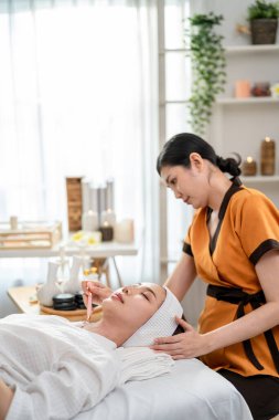 Asyalı genç bir kadın güzellik merkezinde Gua sha ile yüz masajı yaptırıyor. Çekici kız masaj yatağında uzanıyor, masözden fizyoterapi alıyor yüz tedavisinde kırışıklıkları önlemek için masajı kaldırıyor..