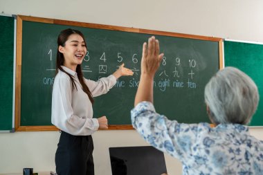 Asyalı bayan eğitmen, dil okulunda yetişkin öğrencilere ders veriyor. Çekici bayan öğretmen öğrencileri motive eder ve açıklar. Yetişkinler için özel ders sırasında yeni beceriler öğrenirler.