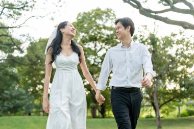 Gün batımında parkta el ele tutuşan Asyalı genç bir çift. Çekici romantik damat ve gelin koşuyor, aşklarını ve sevgililer gününü kutluyorlar, düğün öncesi dışarıda eğleniyorlar..