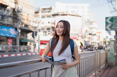 Asyalı güzel bir kadın sırt çantalı sokak şehrinde geziyor. Çekici turist kız yolda yürürken mutlu ve rahatlamış hissediyor, tatil gezisinde boş zamanların tadını çıkarıyor..