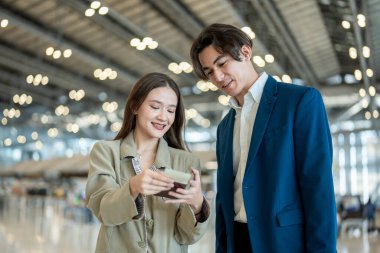 Asyalı işadamı ve kadın havaalanından kalkış biletini kontrol ediyor. Çekici erkek ve kadın yolcu tatil gezisi için uçakla yurtdışına gittikleri için mutlu ve heyecanlı hissediyorlar..