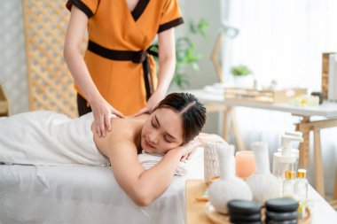 Asyalı genç bir kadın güzellik merkezinde sırt masajı yaptırıyor. Çekici, güzel bir kız masaj yatağında uzanıyor ve masaj salonundaki vücut için masözden rahatlatıcı fizyoterapi hizmeti alıyor.