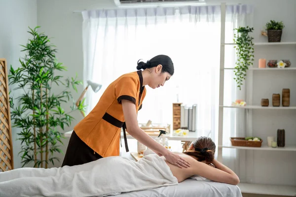 Asyalı genç bir kadın güzellik merkezinde sırt masajı yaptırıyor. Çekici, güzel bir kız masaj yatağında uzanıyor ve masaj salonundaki vücut için masözden rahatlatıcı fizyoterapi hizmeti alıyor.