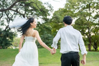 Gün batımında parkta el ele tutuşan Asyalı genç bir çift. Çekici romantik damat ve gelin koşuyor, aşklarını ve sevgililer gününü kutluyorlar, düğün öncesi dışarıda eğleniyorlar..