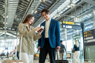 Asyalı işadamı ve kadın havaalanı terminalinden biniş kapısına doğru yürüyorlar. Çekici genç çift, tatil gezisi için uçakla yurtdışına giderken mutlu ve heyecanlı hissediyorlar..