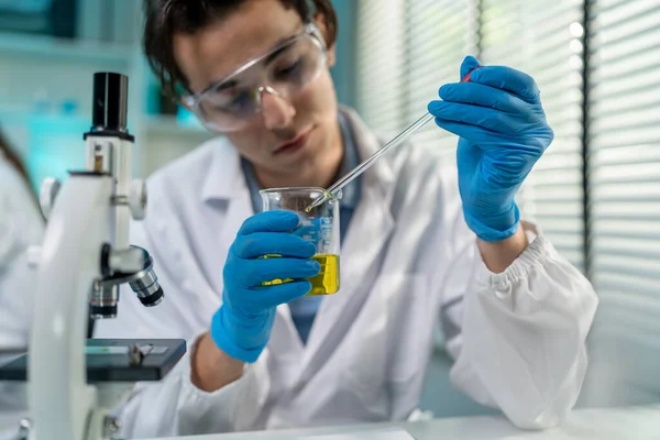 Biyoteknoloji araştırma laboratuvarında çalışan Asyalı erkek bilim adamı. Laboratuvar tüpünde kimyasal bir sıvı tutan çekici teknisyen tıbbi gelişim testleri yapıyor ve analiz ediyor..