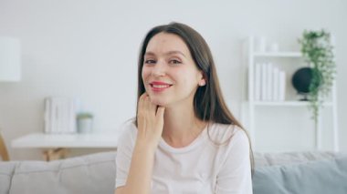 Beyaz kadın evde kameraya gülümsüyor.