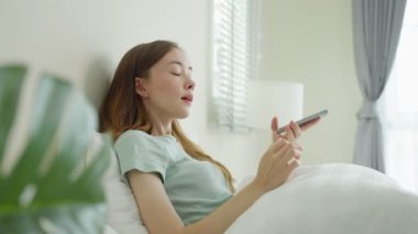 Genç bir kadın akıllı telefon kullanarak yatakta dinleniyor.