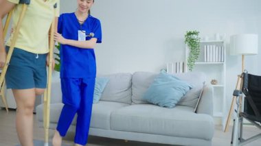 Ev sağlığı ziyareti sırasında bacağından yaralanan hastayı muayene eden önlüklü Asyalı kadın hemşire.