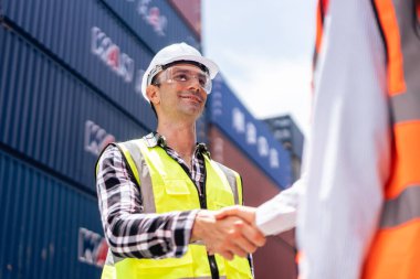 İş kadını ve erkek işçi konteynır terminalinde çalışıyor. Güzel genç kadın ve ustabaşı, kargo gemisindeki depo lojistik talimatlarından sonra el sıkışıyor..