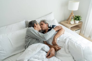 Asyalı yaşlı çift yatağa uzanıyor, sabah öpüşüyorlar. Çekici, olgun, pijamalı kadın ve erkek evdeki yatak odasında sabahın erken saatlerinde eğleniyorlar. Aile ilişkisi kavramı.