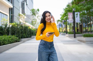 Şehirdeyken kulaklıkla müzik dinlemekten hoşlanan Asyalı bir kadın. Çekici, genç, yetişkin bir kız dışarıda şarkılar dinlerken mutlu ve rahat hissediyor, modern şehir ortamında tek başına seyahat ediyor..