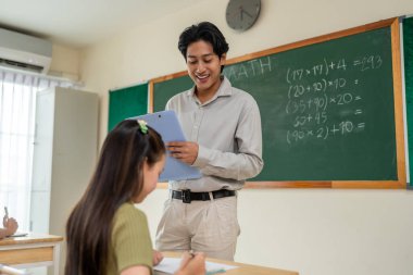 Asyalı öğrenciler ilkokulda öğretmenle birlikte öğreniyorlar. Masada oturan sevimli genç çocuklar, erkek hocalarının öğretmenlerini dinliyorlar ve sınıftaki dersi anlatıyorlar..