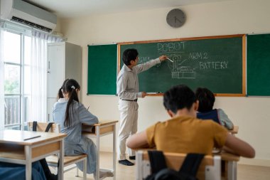 İlkokulda öğretmenle birlikte öğrenen bir grup öğrenci. Masada oturan sevimli genç çocuklar, erkek hocalarının öğretmenlerini dinliyorlar ve sınıftaki dersi anlatıyorlar..