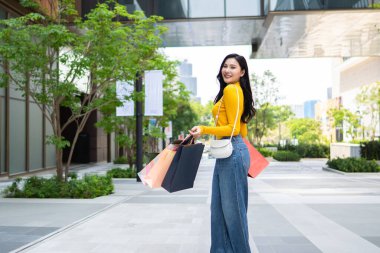 Alışveriş merkezindeki Asyalı kadın eşyalarının portresi. Alışveriş torbaları tutan çekici bir genç kız. Sonra kameraya bakın. Mutlulukla yürürken alışveriş merkezinde alışverişin tadını çıkarın..